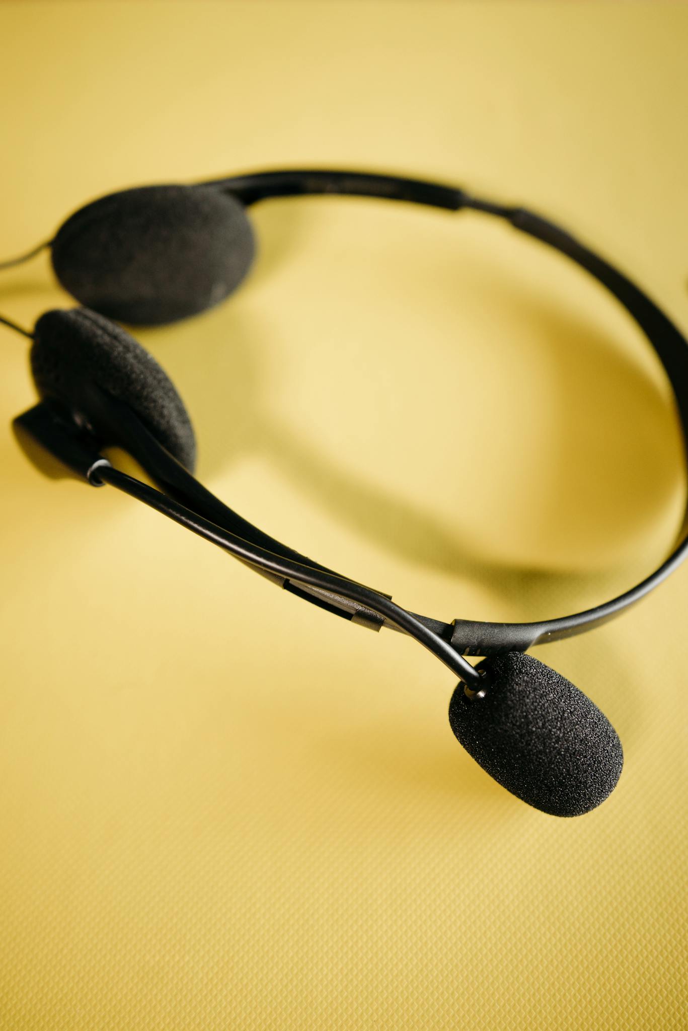 Black headset with microphone resting on a vibrant yellow surface, featuring soft ear cushions.