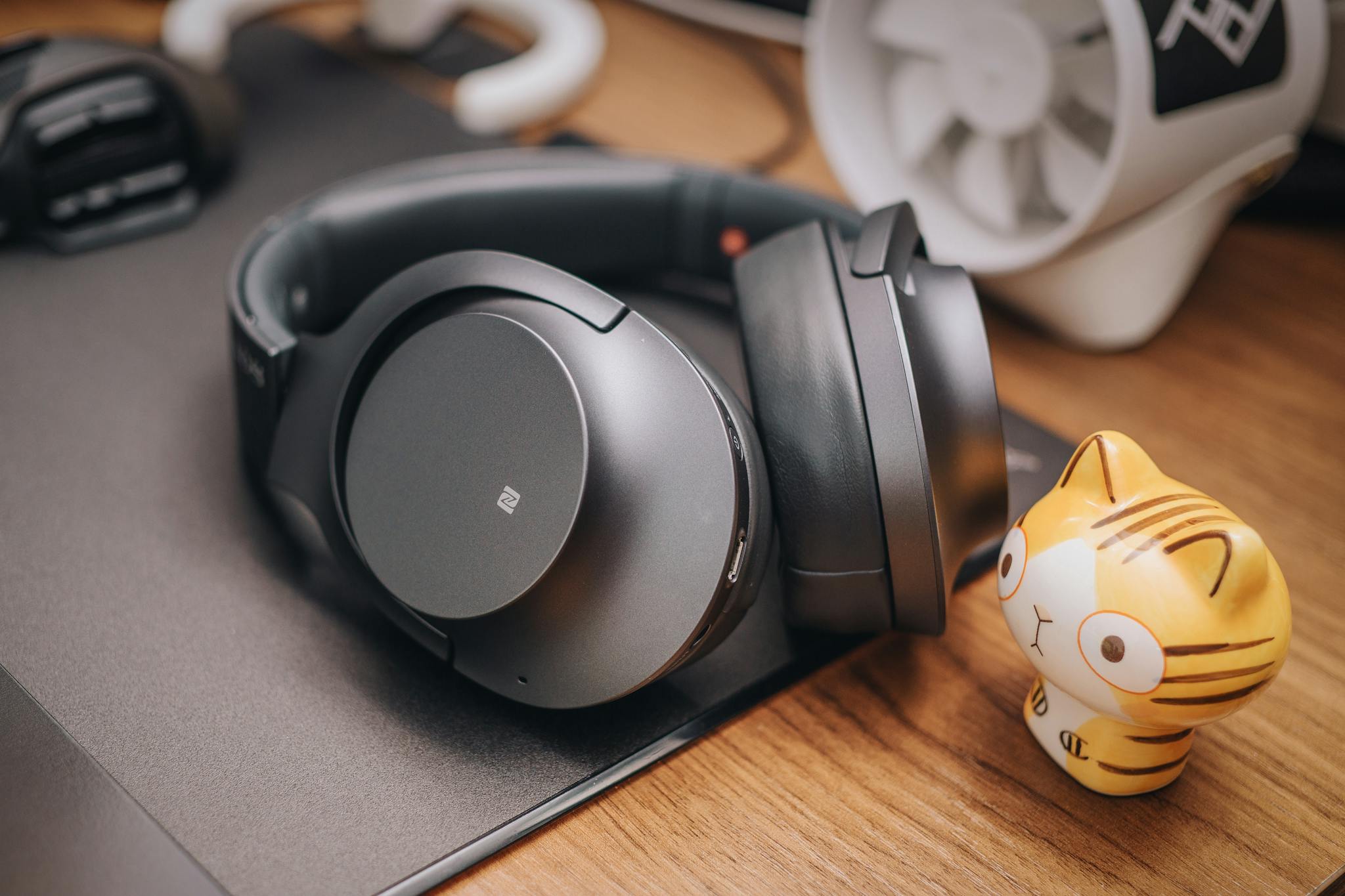 Stylish wireless headphones on a wooden desk with a cute cat figurine. Perfect for tech enthusiasts.